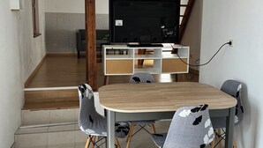 A dining area with a round table, four chairs, a television, and a staircase leading to an upper level.