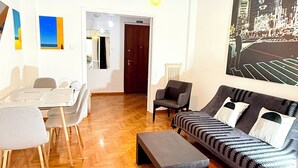 Uma sala de estar moderna com piso de madeira em padrão herringbone, um sofá, uma mesa de jantar com cadeiras e uma luminária pendente.