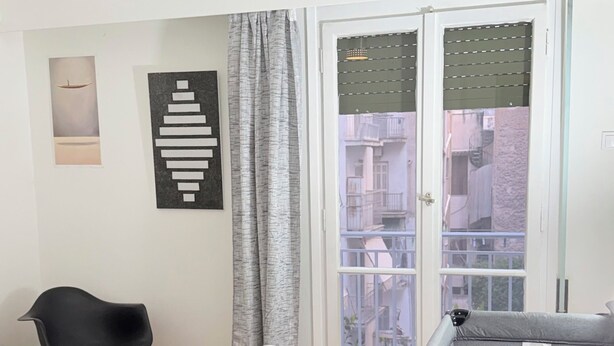 Quarto com cama, uma poltrona, sofá, luminária pendente, janela com persianas e ar condicionado.