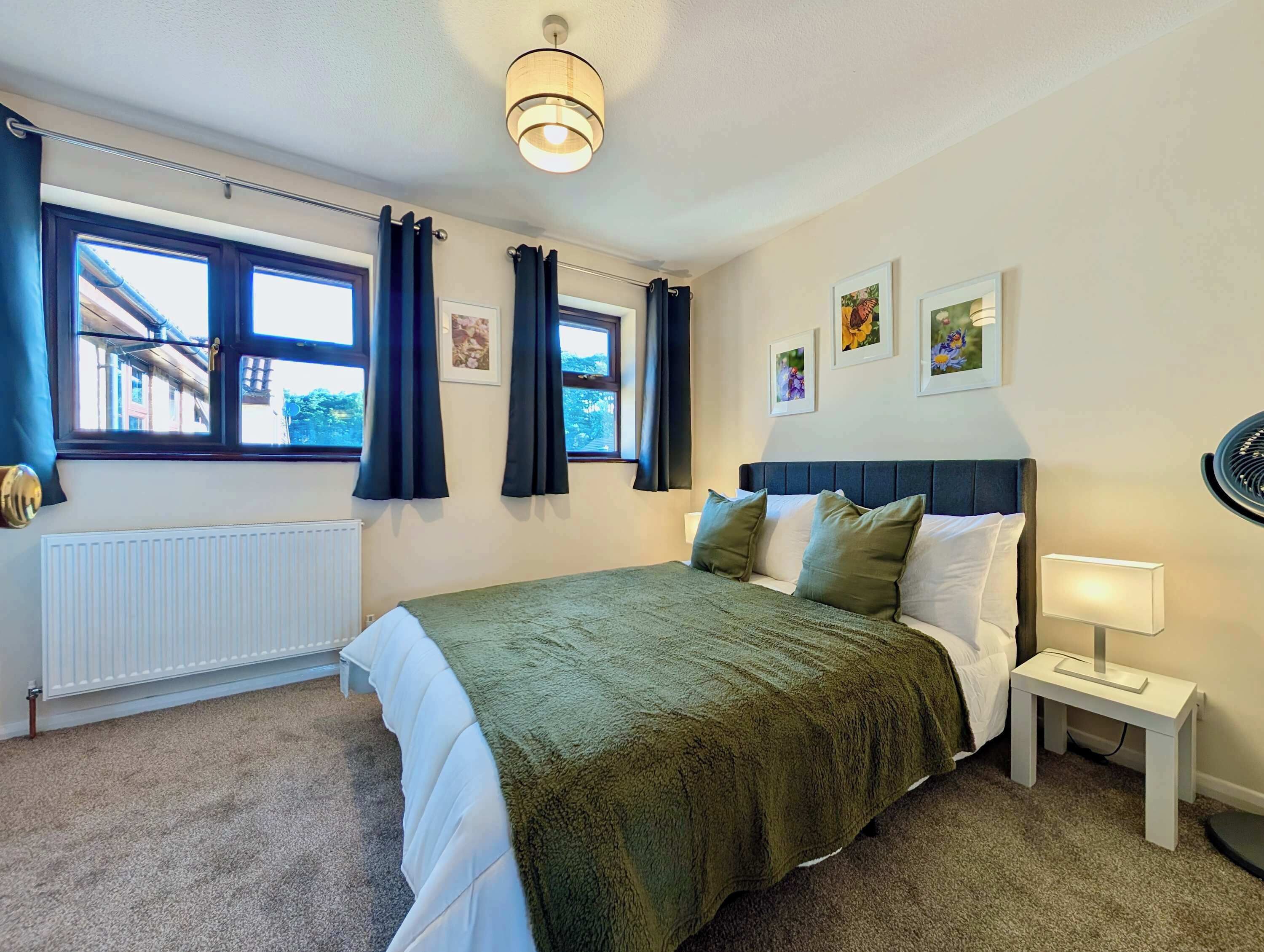 Un dormitorio con cama, radiador, ventana con cortinas, mesita de noche con lámpara y decoración en la pared.