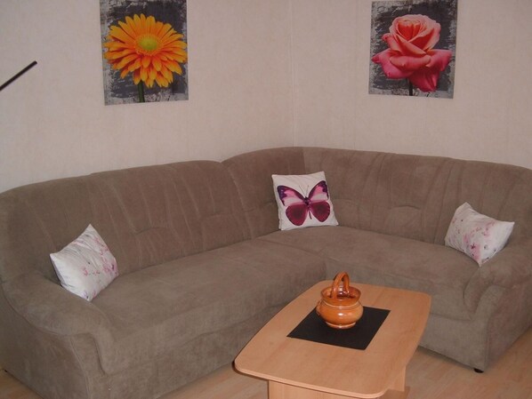A living room with a brown sofa, a small wooden table, and two wall-mounted flower paintings.
