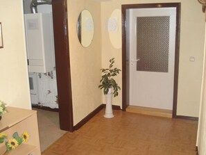 A hallway with a potted plant, a door with a metal screen, and a white wall with a plaque. - Maria Vacation Rental 3 – Cozy, Central, and Ideal for Families (Wernigerode)