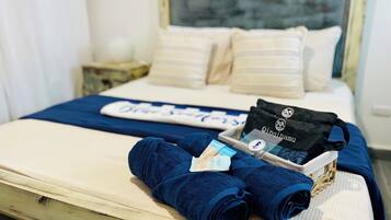 Un lit bien fait, recouvert d’une couverture bleue, une pile de serviettes pliées, un sac noir et un plateau contenant des articles de toilette.