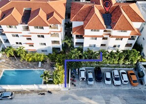 Vista aérea de um edifício residencial com piscina, carros estacionados e céu claro.