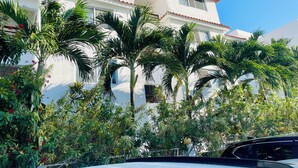 Un edificio de dos pisos con fachada blanca y techo de tejas rojas, rodeado de exuberante vegetación y palmeras.