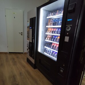 A vending machine with beverages, a door labeled 'WC,' and a wall with a coffee advertisement. - Budget Double Rooms in Vienna (VIENNA)