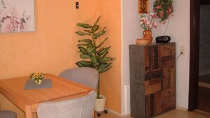 A dining area with a wooden table, grey chairs, a potted plant, a small cabinet, and a hanging plant. - Maria Vacation Rental 1 – Cozy Accommodations with a Warm, Inviting Atmosphere (Wernigerode)