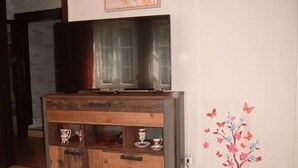 A wooden cabinet with drawers and shelves, a television on top, and a wall with a floral mural. - Maria Vacation Rental 1 – Cozy Accommodations with a Warm, Inviting Atmosphere (Wernigerode)