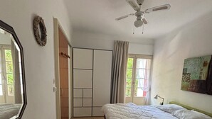 Une chambre avec deux lits, un ventilateur de plafond, un miroir, une armoire et une fenêtre avec des rideaux.