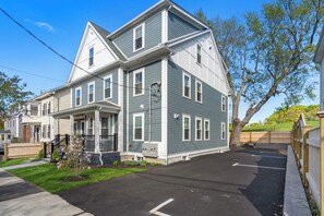 A two-story residential building with a front porch, a driveway, and a fenced yard.