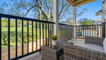 A covered outdoor area with wicker furniture, a wooden deck, and a view of a grassy yard.