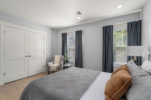 A bedroom with a bed, a chair, a bedside table, and a window with curtains. - New 3 bedroom, 2 bath unit, meadow view! (Boston)