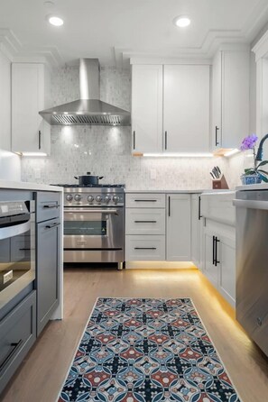 A modern kitchen with stainless steel appliances, white cabinetry, and a patterned rug.