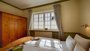 A bedroom with a wooden wardrobe, a bed with white linens, a window with curtains, and a radiator. - Ferienwohnung in Damerow auf Usedom (Koserow)