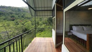 Un balcón con vistas a un paisaje verde exuberante, suelo de madera y una cama con ropa blanca.