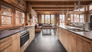Una cucina in stile baita con mobili in legno, forno a incasso, zona pranzo con panche e ampie finestre.