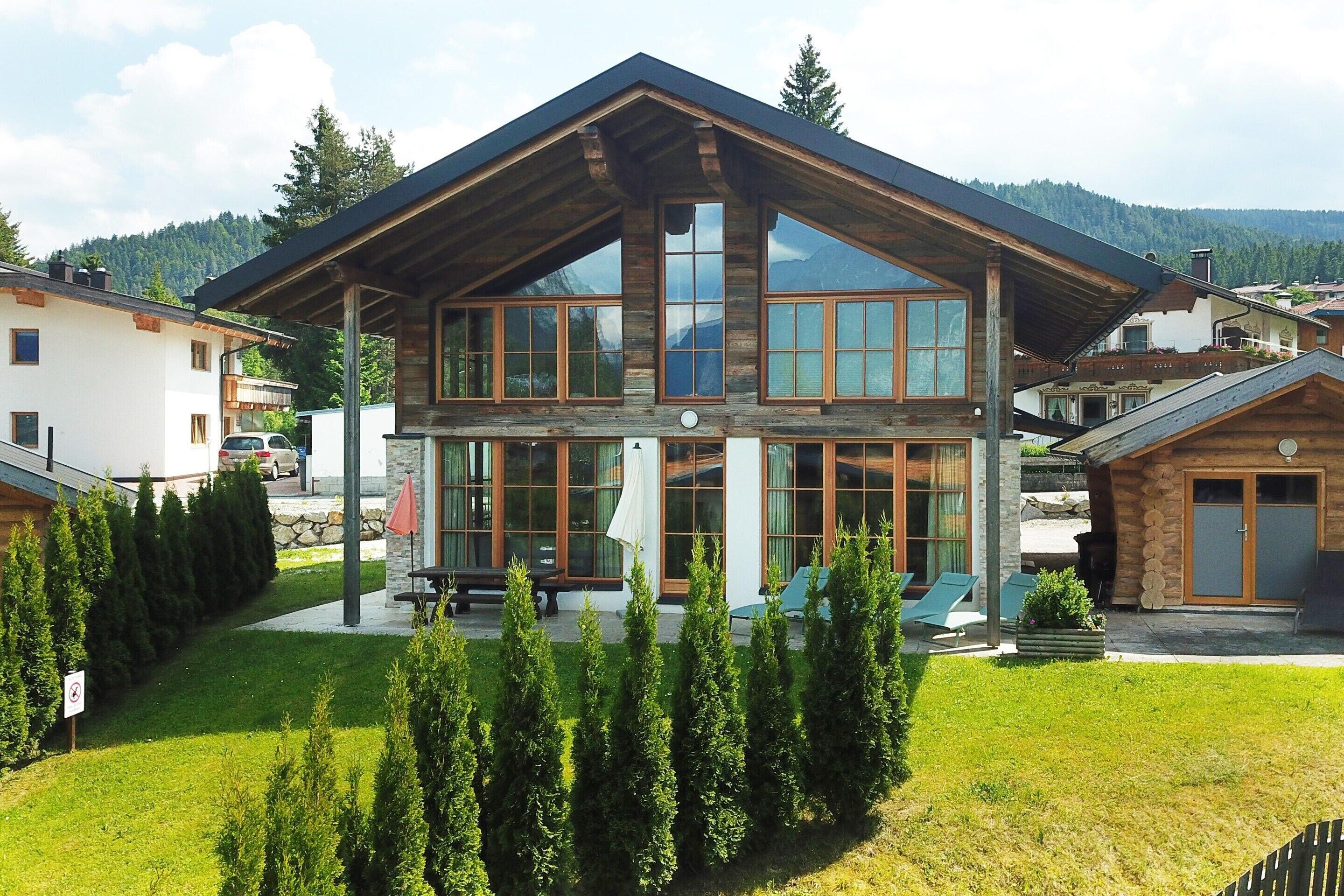 A two-story wooden house with large windows, a covered patio, and a well-maintained lawn.