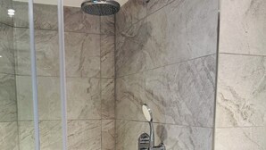 Eine moderne Dusche mit Handbrause und am Wand montiertem Wasserhahn, eingebettet in ein Zimmer mit Marmorfliesen.