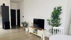 Ein modernes Wohnzimmer mit einem Flachbildfernseher, einem Esstisch und einer großen Pflanze.