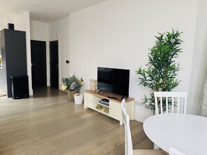 A modern living room with a flat-screen TV, a dining table, and a large plant. - Windsor apartment, sleeps 4, Walking to Castle and River Thames (Windsor)