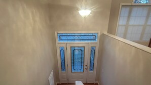 Un escalier menant à une porte ornée de panneaux de vitrail, avec un luminaire placé au-dessus.