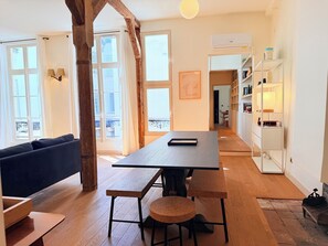 A modern interior with a dining area, a sofa, and a staircase leading to an upper floor. - 3-bedroom 2 bathroom apartment in Le Marais with AC (Paris)