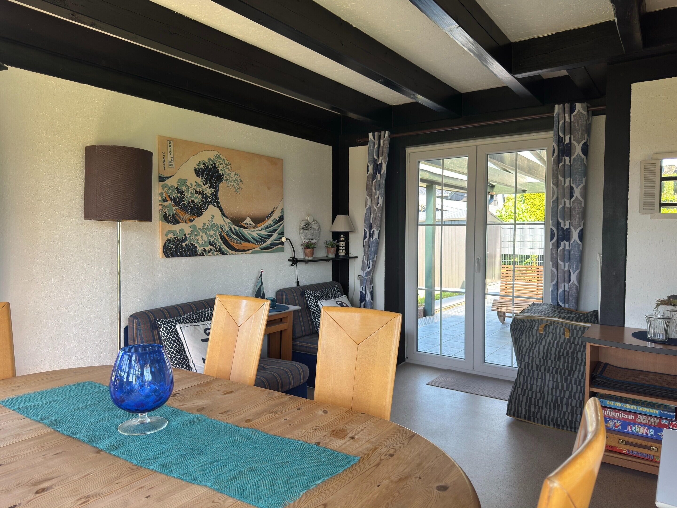 A dining area with a wooden table, chairs, a blue glass vase, and a Japanese wave painting on the wall.