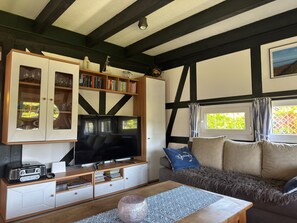 Ein Wohnzimmer mit Fernseher, Bücherregalen, einem Sofa und einem Fenster mit Vorhängen.