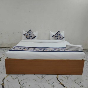 Cama com base de madeira, roupa de cama branca e almofadas estampadas.