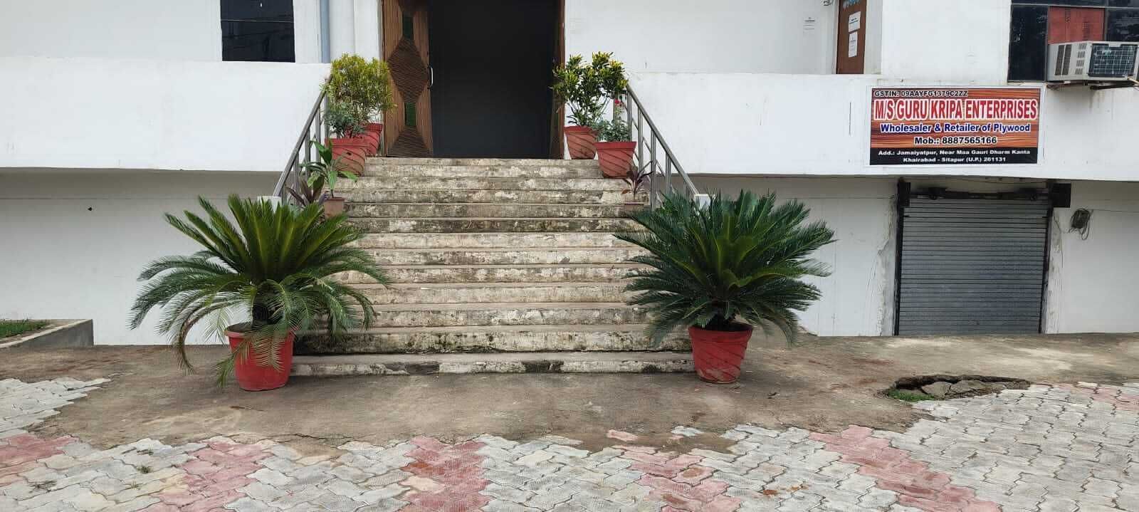 A building with a staircase leading to a door, potted plants on either side, and a signboard on the right.