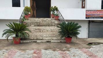 A building with a staircase leading to a door, potted plants on either side, and a signboard on the right.