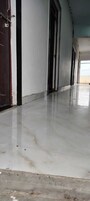 A corridor with a marble floor, a wooden door, and a white wall.