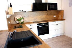 Eine moderne Küche mit Holzausziehtisch, schwarzem Spülbecken, weißen Schränken und einem eingebauten Backofen.