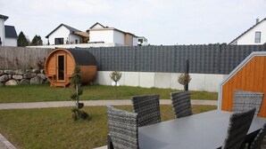 A patio with a table and chairs, a wooden barrel, a small tree, and a shed in a residential backyard. - Semi-detached house for groups with 4 bedrooms (Jesendorf)