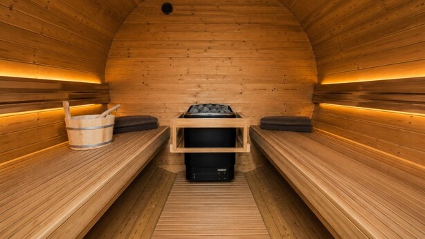 A sauna with wooden benches, a wooden bucket, and a black heater. - Semi-detached house for groups with 4 bedrooms (Jesendorf)