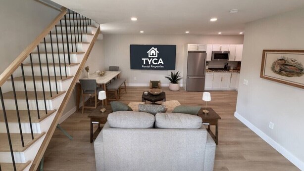 Un appartement moderne avec un escalier, un coin repas, un salon avec un canapé et une cuisine à l’arrière-plan.