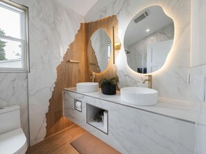 Ein Badezimmer mit Marmorwaschtisch, einer Holzwand und einem großen Spiegel.
