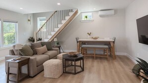 Un salon moderne avec un escalier, un coin repas et un téléviseur à écran plat fixé au mur.