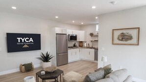 Un appartement moderne doté d’une kitchenette, d’un espace de vie avec un canapé et une table basse, et d’un téléviseur à écran plat fixé au mur.