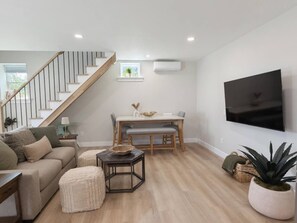 Ein modernes Wohnzimmer mit Treppe, Essbereich und an der Wand befestigtem Flachbildfernseher.