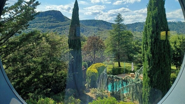 A view through a window of a lush garden with tall trees, a clear sky, and distant hills. - Eco-Honeymoon - 10 min. from the Bamboo Garden - for 4, 6, or 8 people (Anduze)