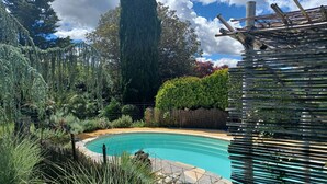 Une piscine entourée d’une végétation luxuriante, d’un grand arbre et d’une clôture en bois.