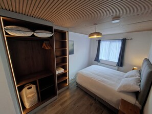 Ein Schlafzimmer mit Bett, Kleiderschrank mit Regalen, einem Fenster mit Vorhängen und einer Deckenleuchte.