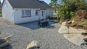Et etplanshus med tegltag, grusindkørsel og en lille terrasse med bord og stole.