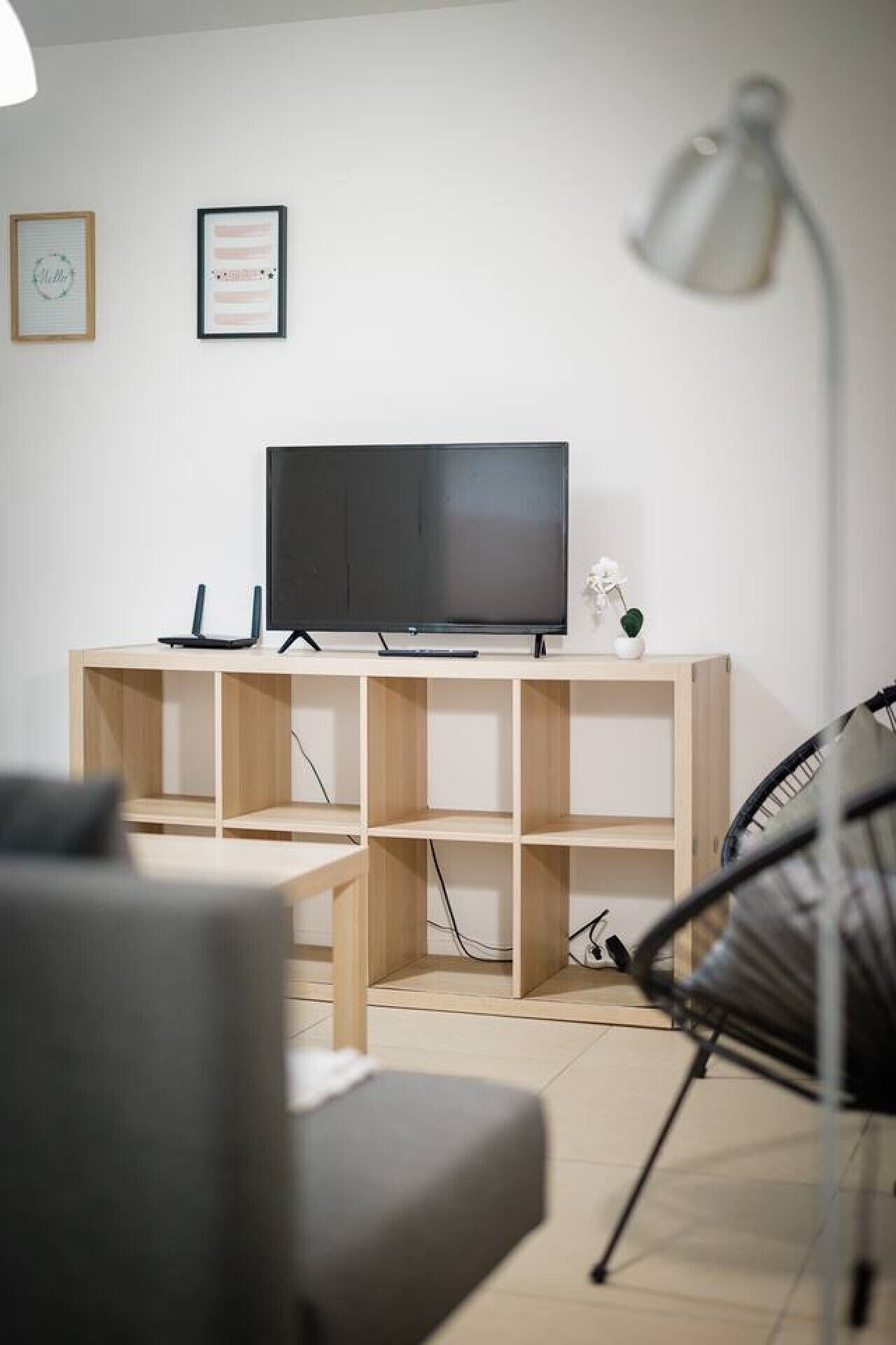 Ett modernt vardagsrum med en platt-TV på ett TV-bord i trä, en grå soffa, en svart fåtölj och en golvlampa.