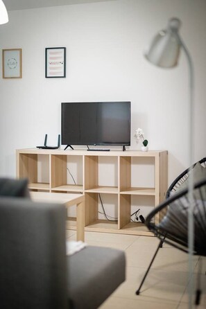 Ett modernt vardagsrum med en platt-TV på ett TV-bord i trä, en grå soffa, en svart fåtölj och en golvlampa.