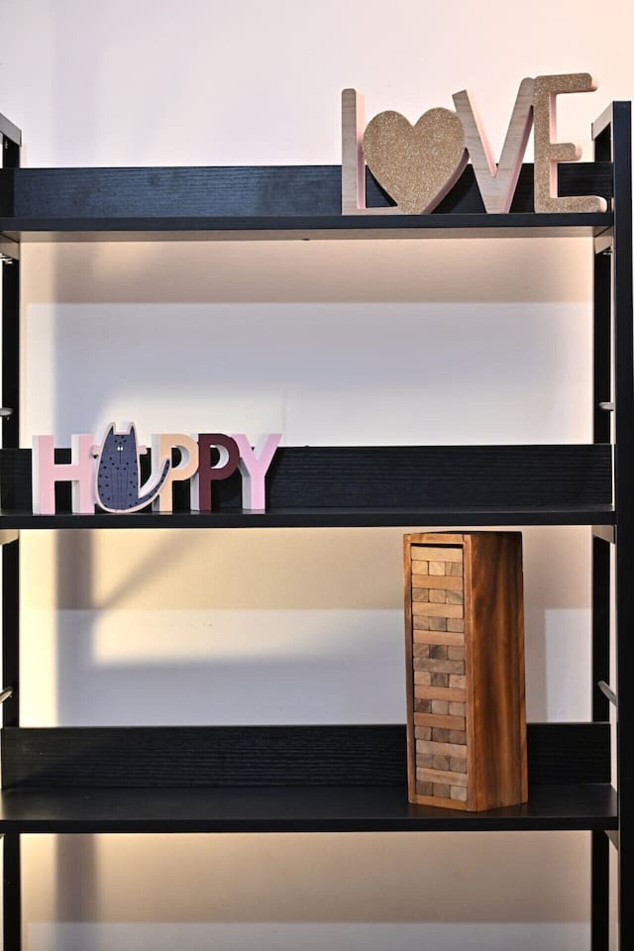 Een zwart schap met decoratieve letters die 'LOVE' en 'HAPPY' spellen op het bovenste plank, en een houten blok op het onderste plank.