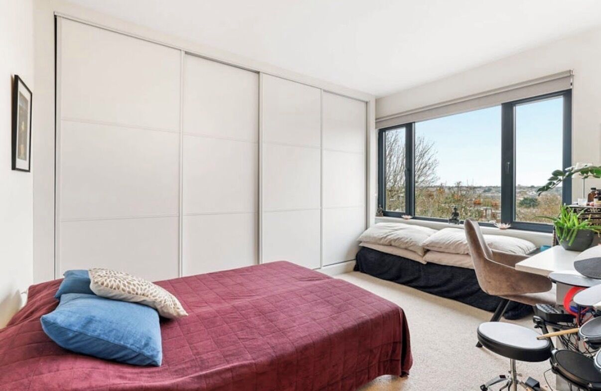 A bedroom with a bed, a desk with a chair, a window with a view, and a sliding door.
