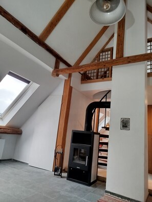 A room with a sloped ceiling, a built-in wood beam structure, a black wood stove, a skylight, and a staircase leading to an upper level. - BergwaldHaus Willingen, Diemelsee, Winterberg (Brilon)