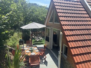 Une terrasse avec une table dressée pour les repas, un barbecue et un espace couvert avec des chaises.